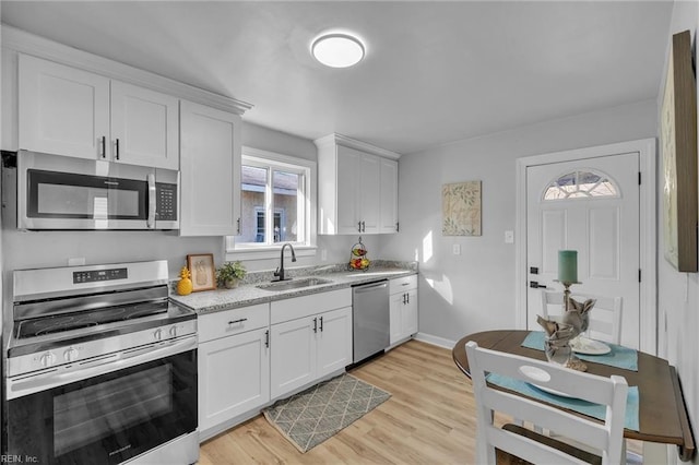 kitchen with light stone countertops, stainless steel appliances, sink, light hardwood / wood-style flooring, and white cabinetry