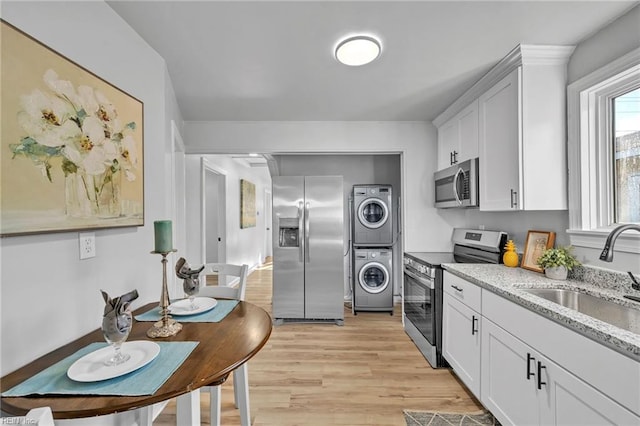 kitchen with appliances with stainless steel finishes, sink, light hardwood / wood-style flooring, stacked washer and clothes dryer, and white cabinetry