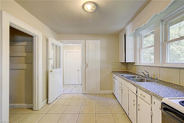 kitchen with sink, stainless steel stove, light tile patterned flooring, decorative backsplash, and white cabinets