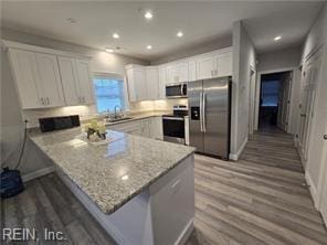 kitchen featuring kitchen peninsula, white cabinetry, light stone counters, and appliances with stainless steel finishes