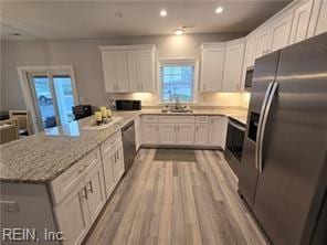 kitchen with white cabinets, sink, light stone countertops, appliances with stainless steel finishes, and light hardwood / wood-style floors