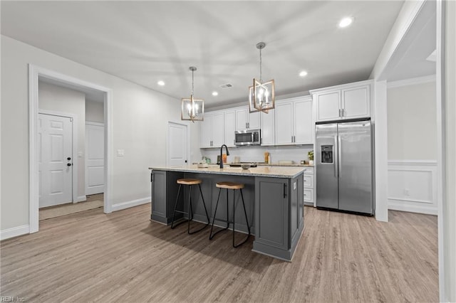 kitchen with appliances with stainless steel finishes, a center island with sink, light hardwood / wood-style floors, white cabinetry, and hanging light fixtures