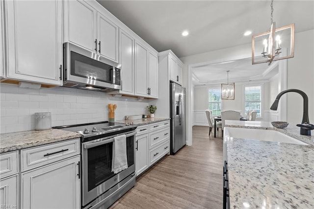 kitchen featuring pendant lighting, white cabinets, crown molding, light hardwood / wood-style floors, and stainless steel appliances