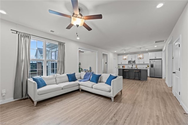 living room featuring ceiling fan, sink, and light wood-type flooring