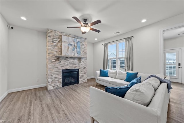 living room featuring ceiling fan, a stone fireplace, and light hardwood / wood-style flooring