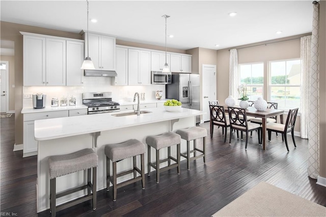 kitchen featuring sink, stainless steel appliances, dark hardwood / wood-style floors, decorative light fixtures, and a kitchen island with sink