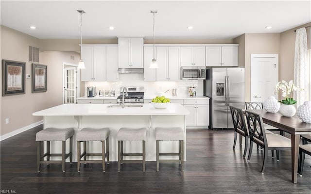 kitchen featuring stainless steel appliances, a kitchen island with sink, sink, white cabinets, and hanging light fixtures