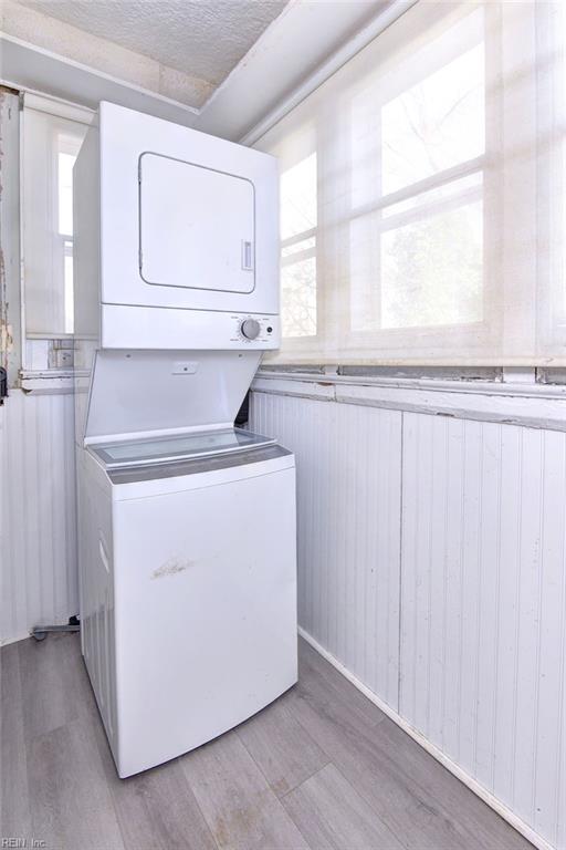 washroom featuring a textured ceiling, wooden walls, stacked washer and clothes dryer, and light wood-type flooring