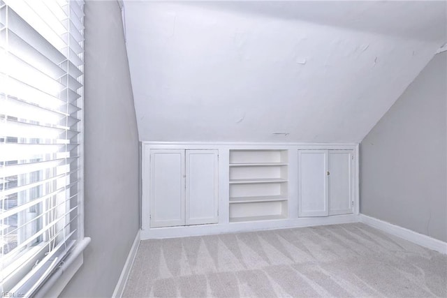 bonus room featuring built in features, light colored carpet, and lofted ceiling