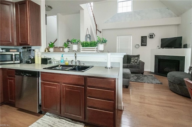 kitchen featuring kitchen peninsula, appliances with stainless steel finishes, sink, high vaulted ceiling, and light hardwood / wood-style flooring