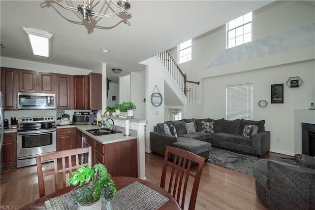 kitchen with sink, a towering ceiling, a chandelier, appliances with stainless steel finishes, and light wood-type flooring