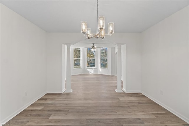 unfurnished dining area featuring ornate columns, ceiling fan with notable chandelier, and light wood-type flooring