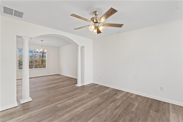 empty room featuring ceiling fan with notable chandelier, wood-type flooring, and decorative columns