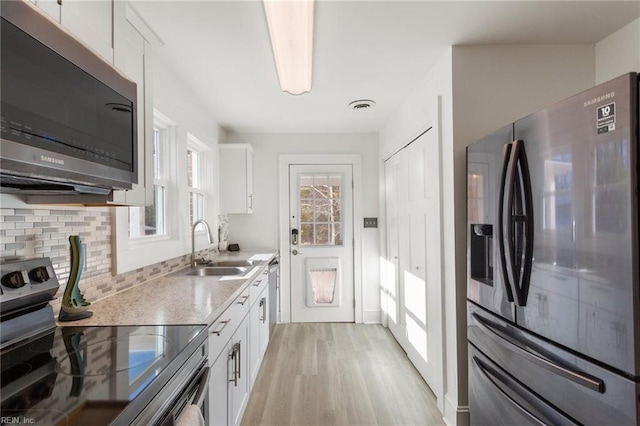 kitchen with white cabinets, sink, tasteful backsplash, light hardwood / wood-style floors, and stainless steel appliances