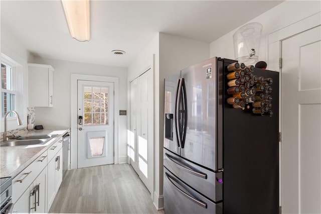 kitchen featuring white cabinets, sink, light hardwood / wood-style flooring, light stone counters, and stainless steel appliances