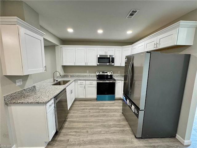 kitchen featuring sink, light stone counters, appliances with stainless steel finishes, white cabinets, and light wood-type flooring