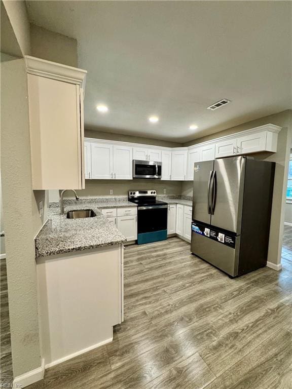 kitchen with white cabinets, sink, light stone countertops, light wood-type flooring, and appliances with stainless steel finishes