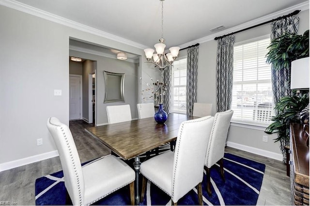 dining area featuring dark wood-type flooring, ornamental molding, and a notable chandelier