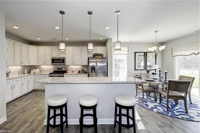 kitchen with pendant lighting, a center island, hardwood / wood-style flooring, white cabinetry, and stainless steel appliances