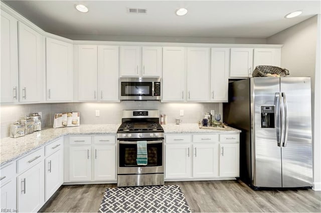 kitchen featuring white cabinetry, light stone counters, backsplash, appliances with stainless steel finishes, and light wood-type flooring