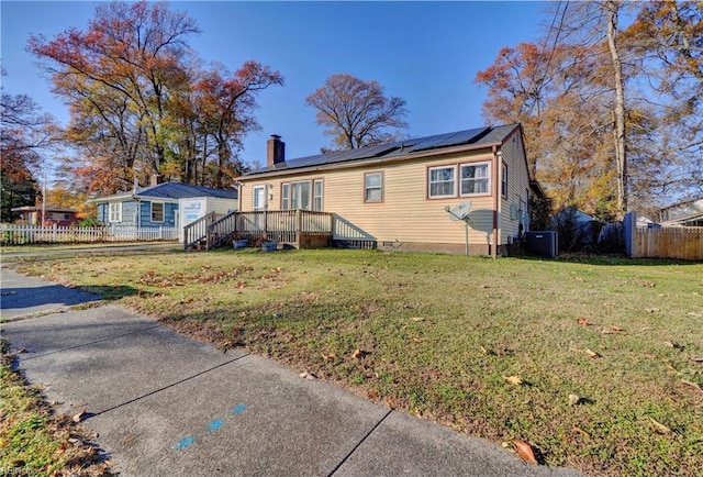 view of front of house with a front yard, solar panels, cooling unit, and a wooden deck