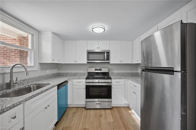 kitchen with light stone countertops, appliances with stainless steel finishes, light wood-type flooring, sink, and white cabinets