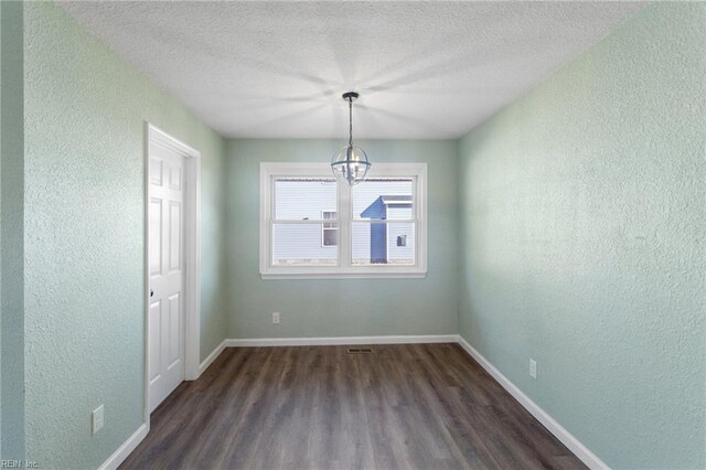 empty room featuring a textured ceiling, an inviting chandelier, and dark wood-type flooring