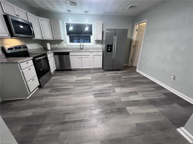 kitchen with dark wood-type flooring, light stone counters, white cabinets, stainless steel appliances, and a sink