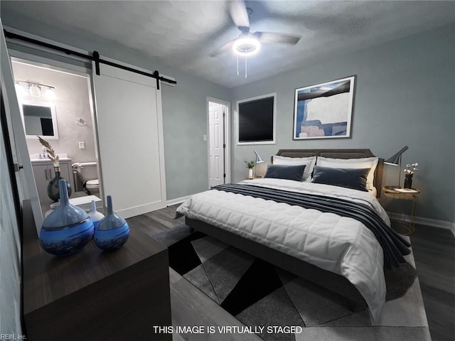 bedroom with a ceiling fan, dark wood-style floors, connected bathroom, a barn door, and baseboards