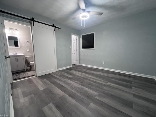 unfurnished bedroom featuring dark wood-style floors, baseboards, ensuite bath, and a barn door