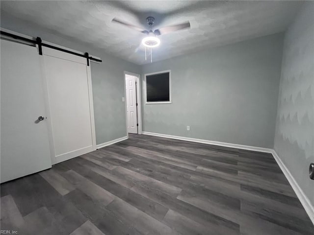 unfurnished bedroom with ceiling fan, baseboards, dark wood finished floors, a barn door, and a textured ceiling