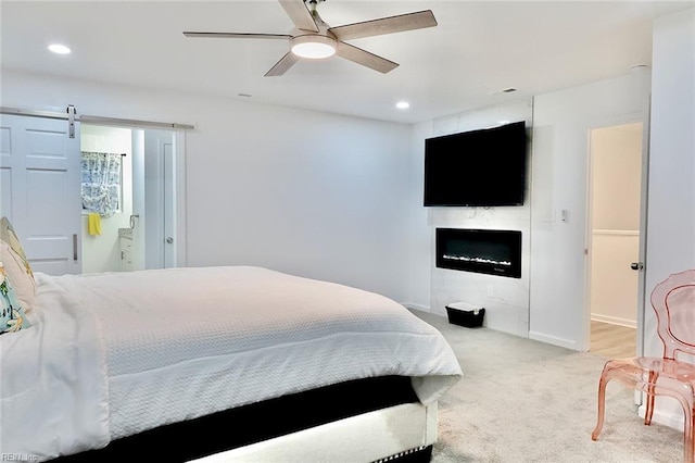 bedroom with light carpet, a barn door, ensuite bath, and ceiling fan