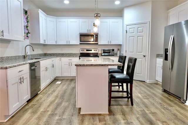 kitchen featuring a center island, decorative light fixtures, light stone counters, white cabinetry, and stainless steel appliances