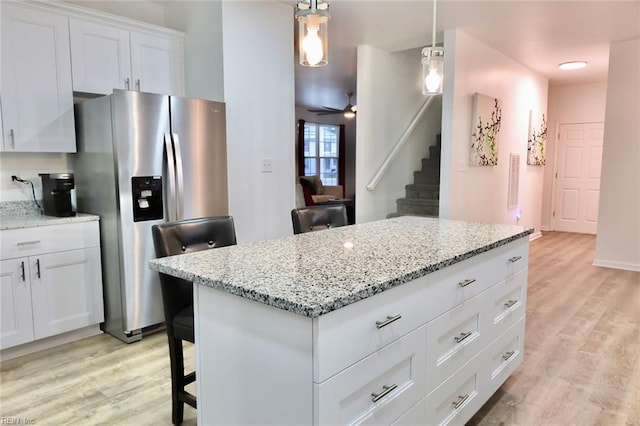 kitchen featuring white cabinets, a kitchen breakfast bar, hanging light fixtures, stainless steel fridge, and light hardwood / wood-style floors