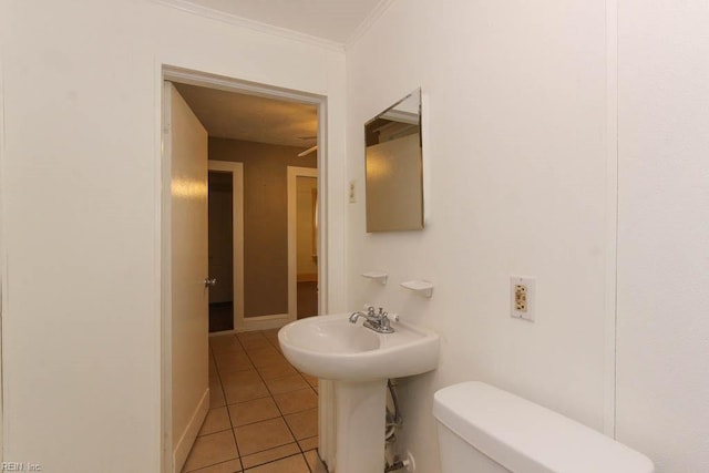 bathroom featuring crown molding, toilet, a sink, baseboards, and tile patterned floors