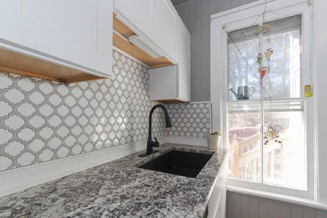 kitchen featuring stone countertops, a sink, white cabinets, and decorative backsplash