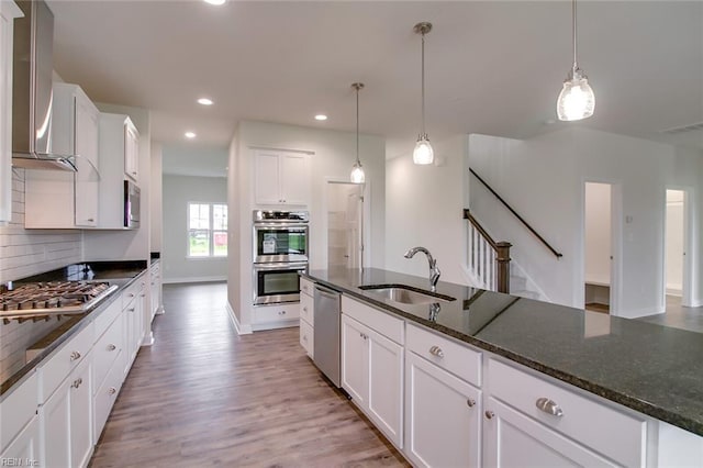 kitchen with white cabinets, wall chimney exhaust hood, sink, and stainless steel appliances