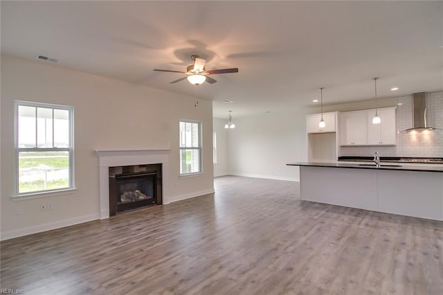 unfurnished living room with ceiling fan with notable chandelier, light hardwood / wood-style floors, and sink