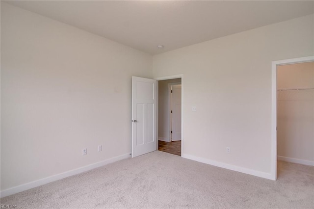 unfurnished bedroom featuring a spacious closet, a closet, and light colored carpet