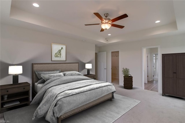 carpeted bedroom featuring a tray ceiling, ensuite bath, and ceiling fan