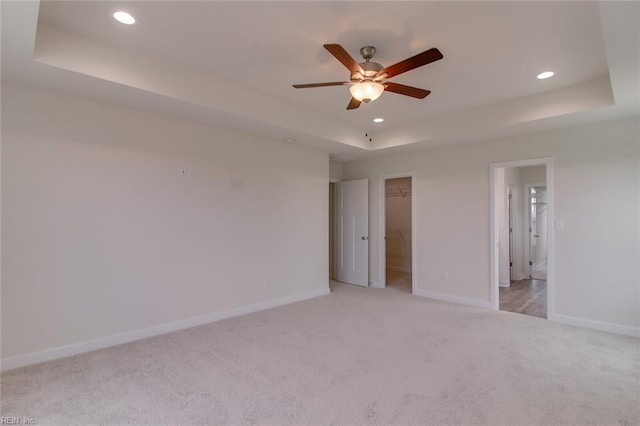 unfurnished room featuring a raised ceiling, light carpet, and ceiling fan