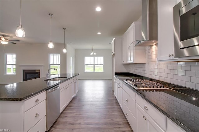 kitchen featuring dark stone countertops, sink, wall chimney range hood, and appliances with stainless steel finishes