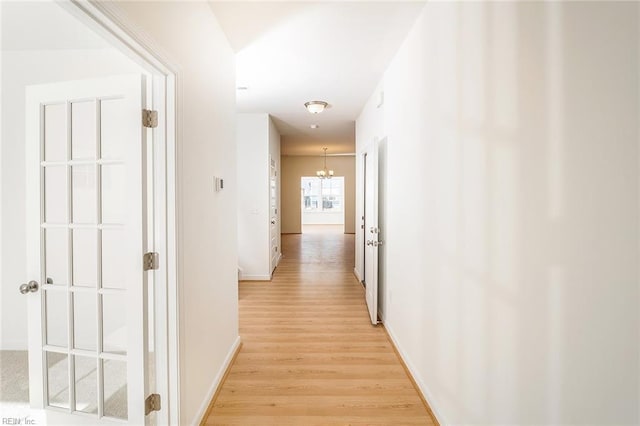 corridor with light wood-type flooring and an inviting chandelier