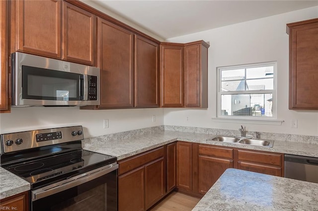 kitchen featuring light stone countertops, sink, light wood-type flooring, and appliances with stainless steel finishes