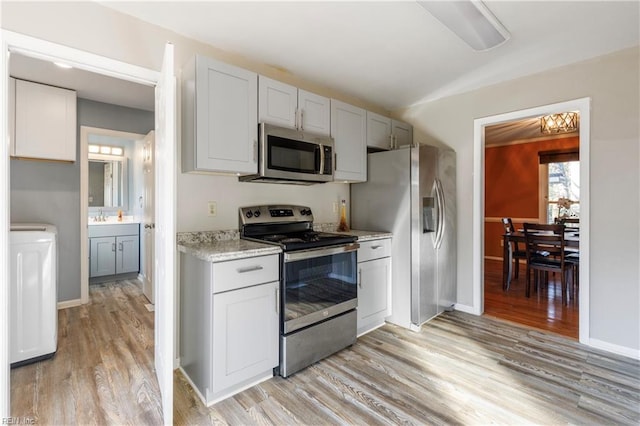 kitchen with white cabinets, stainless steel appliances, light hardwood / wood-style flooring, and light stone counters