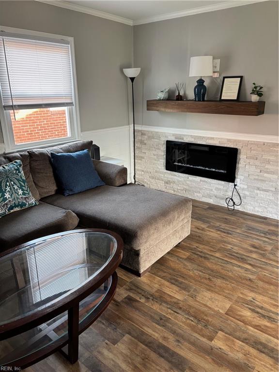 living room featuring a stone fireplace, crown molding, and dark hardwood / wood-style flooring