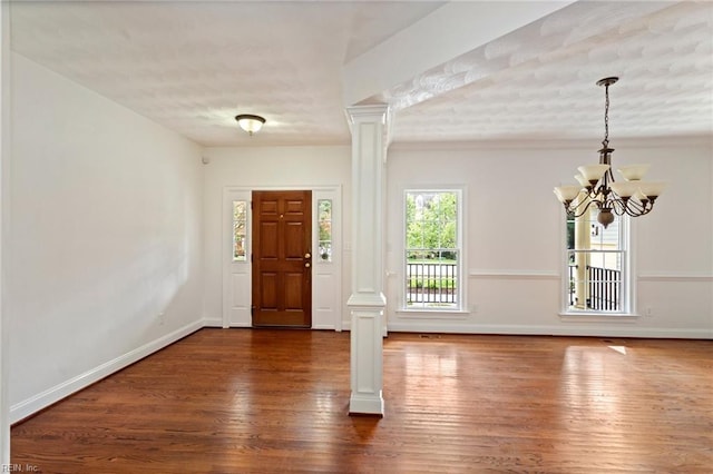 entrance foyer with decorative columns, dark wood-type flooring, and a notable chandelier