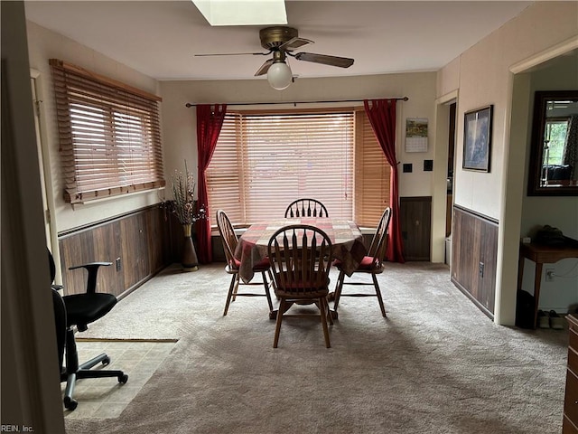 carpeted dining room featuring ceiling fan and wood walls