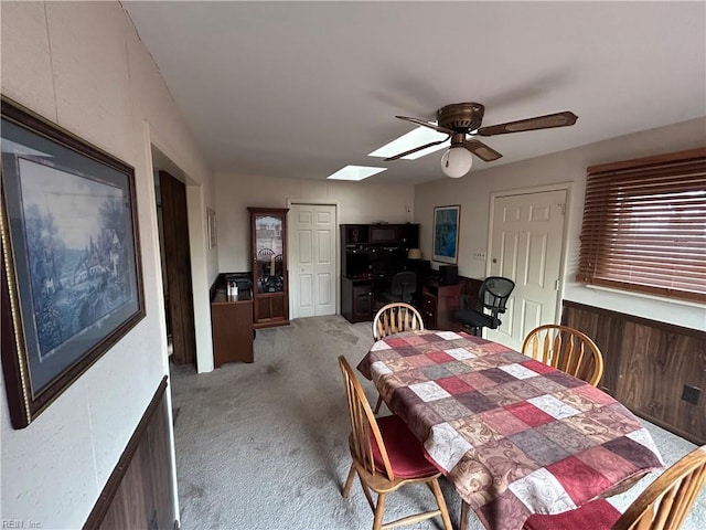 carpeted dining space with a skylight, ceiling fan, and wood walls