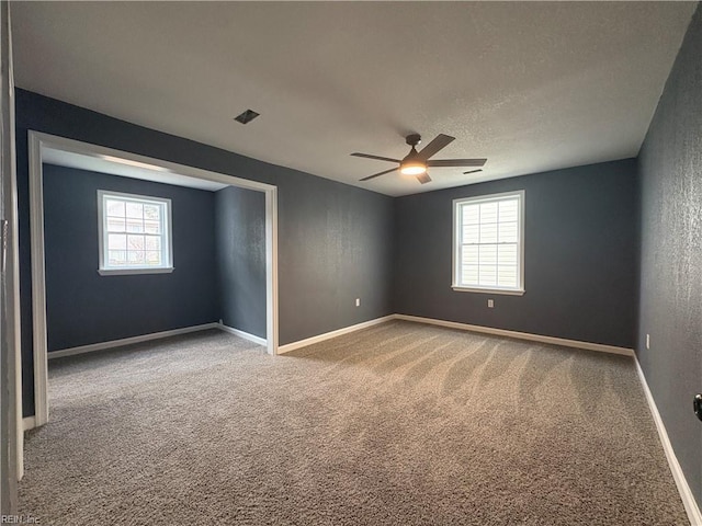 carpeted spare room featuring a textured ceiling, a wealth of natural light, and ceiling fan